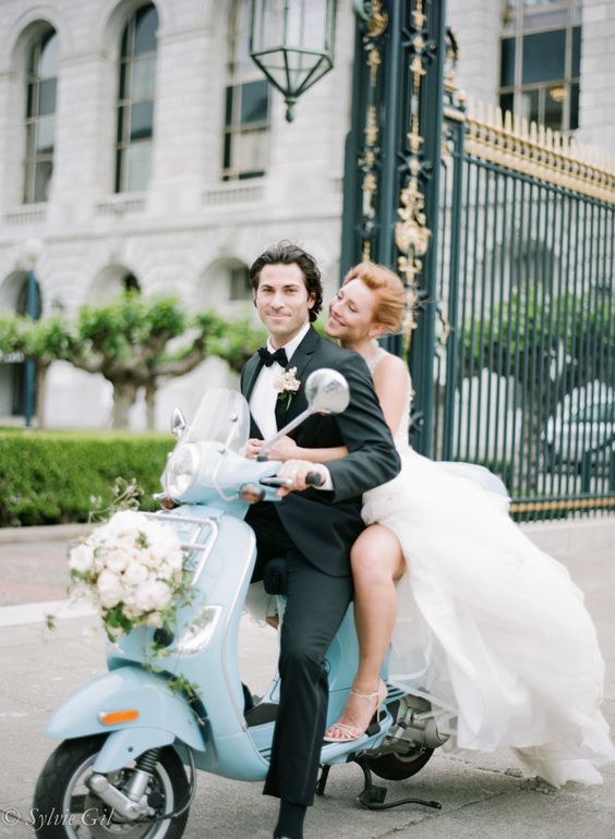 Riding off from their wedding on a flowered, blue Vespa