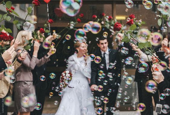 friends celebrating just married couple with soap bubbles and red roses by Nox | Stocksy United